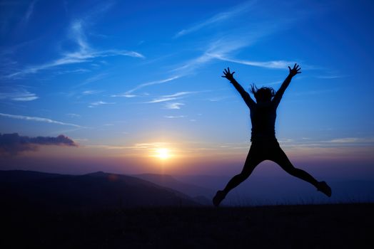 Silhouette of young woman jumping against sunset