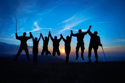 Silhouette of jumping friends in sunset against blue sky