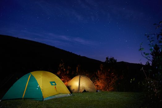 Illuminated yellow camping tent under stars at night