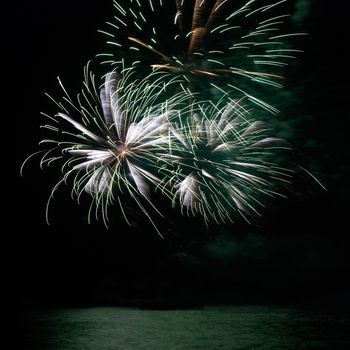 Green colorful holiday fireworks on the black sky background.