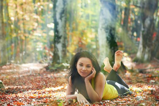 Pretty girl in the autumn forest laying on yellow leaves