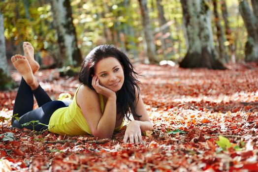 Pretty girl in the autumn forest laying on yellow leaves