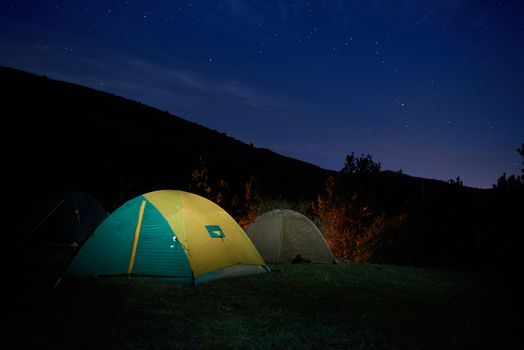 Illuminated yellow camping tent under stars at night