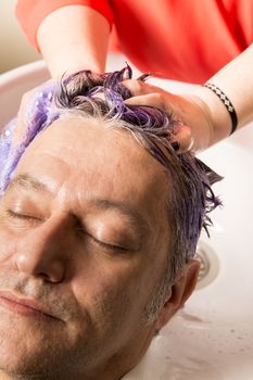 Close up of face of man is getting a hairwash by a hairdresser, with relaxation. The beautician is making foam from shampoo