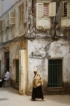 Stone Town, Tanzania - December 30, 2015: Woman in traditional Muslim clothes walking on the street of Stone Town. Background is another house.