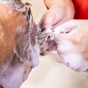 Close up of face of man is getting a hairwash by a hairdresser, with relaxation. The beautician is making foam from shampoo