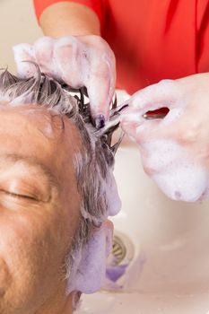 Close up of face of man is getting a hairwash by a hairdresser, with relaxation. The beautician is making foam from shampoo