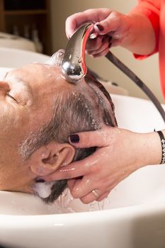 Close up of face of man is getting a hairwash by a hairdresser, with relaxation. The beautician is making foam from shampoo