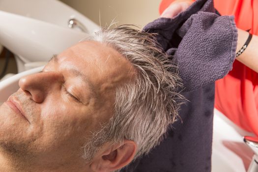 Close up of face of man is getting a hairwash by a hairdresser, with relaxation. The beautician is making foam from shampoo