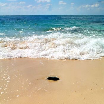 Stone in the sand and the wave behind it.