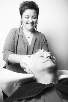 Close up of face of man is getting a hairwash by a hairdresser, with relaxation. The beautician is making foam from shampoo