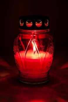 Closeup of red burning votive candle in the dark