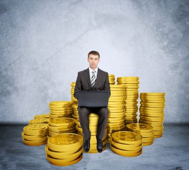 Businessman working on laptop and sitting coins on grey wall background