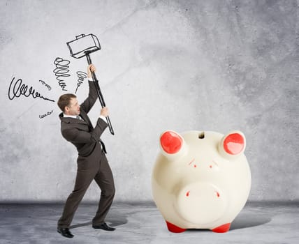 Businessman with hammer and white piggy bank on grey wall background