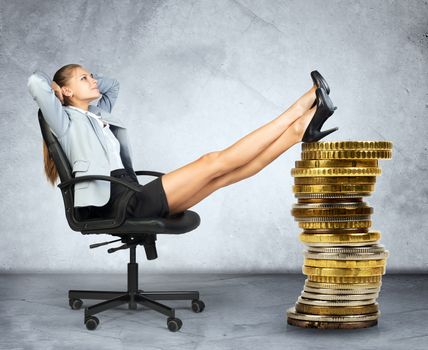 Businesswoman sitting on chair and gold coins on grey background
