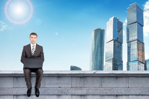 Businessman working on laptop and sitting on roof and looking at camera, front view