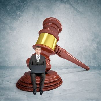 Businessman working on laptop with gavel on grey wall background