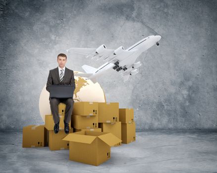 Businessman working on laptop and sitting on pile of boxes and jet