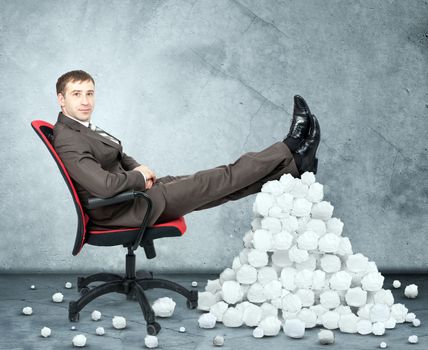 Businessman sitting on chair and pile crumpled paper balls on grey background