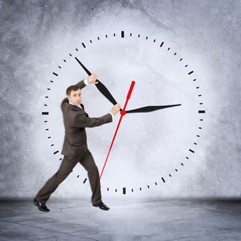 Businessman holding black clock hand and looking at camera on grey wall backgound