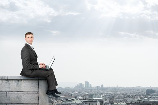 Businessman working on laptop and sitting on roof and looking at camera
