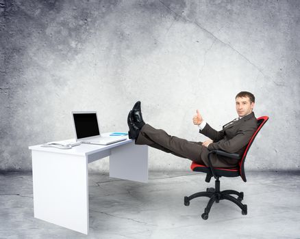 Businessman sitting on chair with table and laptop with legs upon grey background