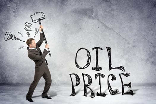 Businessman with hammer and word oil price on grey wall background