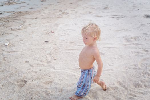 Toddler in a blue pants walking on a white sand in Thailand