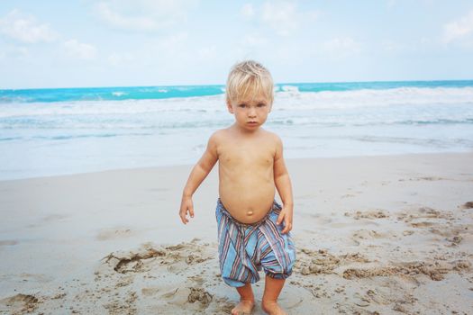 Little boy walking barefoot on white sand beach
