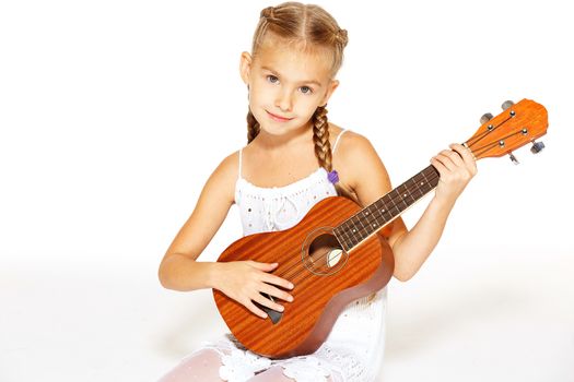 A beautiful little girl with a charming smile in a white dress with a guitar
