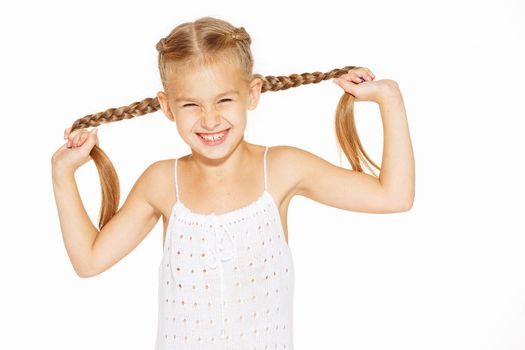 Funny little girl with a charming smile in a white dress holding a pigtails