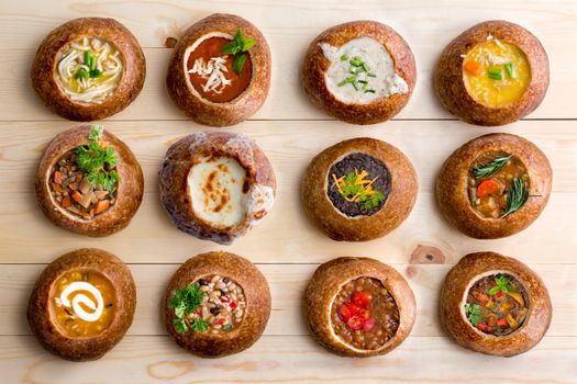 High Angle View of Various Comforting and Savory Gourmet Soups Served in Hollowed Out Bread Bowls on Wooden Table Surface