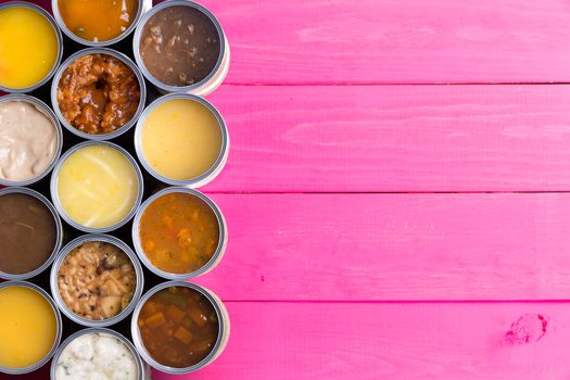 High Angle View of Open Cans of Soup in Wide Variety of Flavors on Bright Pink Painted Wooden Background with Ample Copy Space