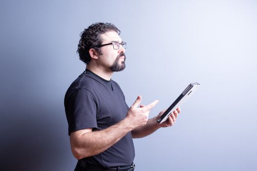 Profile of Man Wearing T-Shirt and Eyeglasses Deep in Thought While Holding Computer Tablet in Studio with Gray Background, Side Lighting and Copy Space