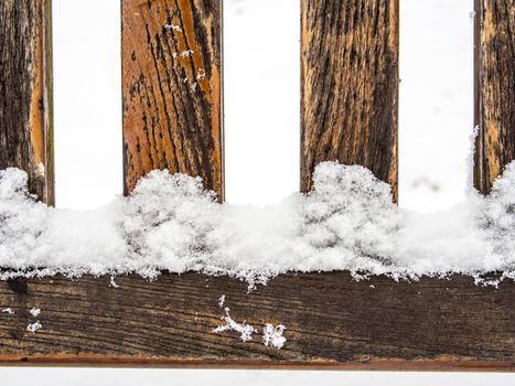 Detail of weathered wooden bench covered in snow, four rungs or spokes, geometrical vertical and horizontal lines, winter time illustration