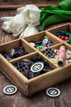 wooden box with buttons and thread on the background of bouquet of white tulips. image is tinted in vintage style