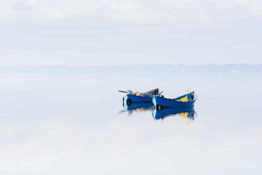 A pair of blue boats remain anchored in the middle of the lagoon. dawn twilight. In the background the island of Sant'Antioco, Sardinia Southwest. Lagoon Bruncu Teula.