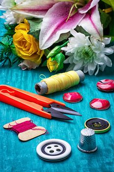 sewing accessories with bouquet of fresh flowers on turquoise background