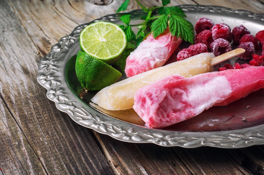 Popsicles served with raspberries and lime on a metal tray.Selective focus