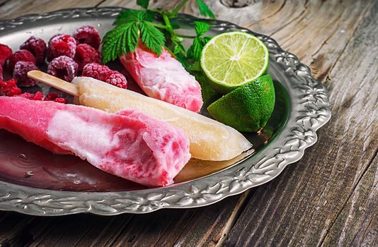 Popsicles served with raspberries and lime on a metal tray.Selective focus