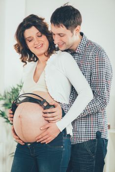 Beautiful happy young couple holding headphones to naked belly pregnant belly. 