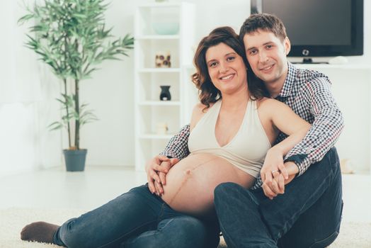 Portrait of a beautiful young couple cuddling the woman's pregnant belly. They smiling and looking at camera.