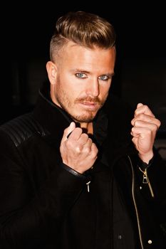 Portrait of a fashionable young man with blue eyes, stylish haircut and posing with a black jacket. Close up. Vertical image.