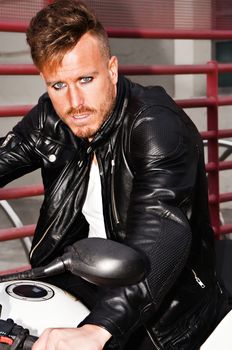 Trendy young man with black leather jacket on a motorcycle with a defiant look. Vertical image.