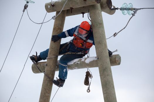 electrician working on top of an electricity pylon with the use of claws-manholes and belt webbing-type