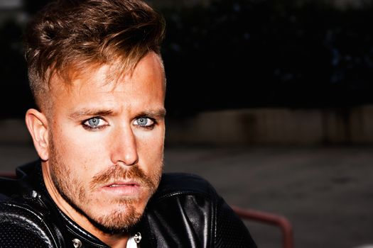 Portrait of a fashionable young man with blue eyes, stylish haircut and posing with a black jacket. Close up. Copy-space. Horizontal image.