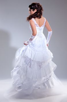 Young beautiful brunette in fashionable wedding dress on isolated studio background