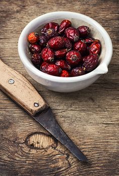 dish of dried medicinal rose hips on background of knife in rustic style