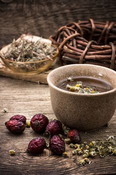 old iron mug of tea and dried berries of the wild rose on wooden table 