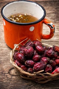 old iron mug of tea and dried berries of the wild rose on wooden table 